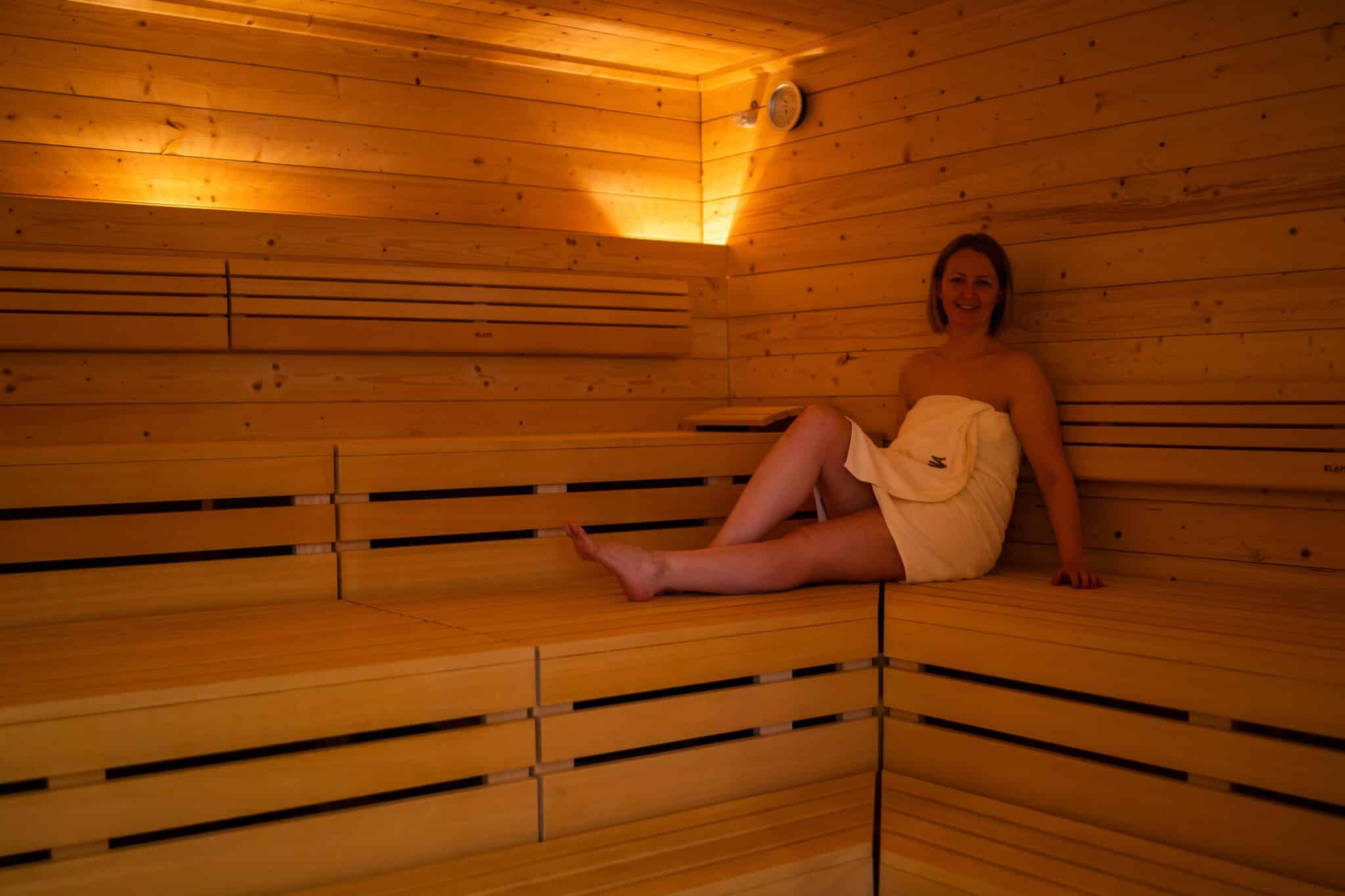 Eine Person sitzt in einer Sauna auf einer Holzbank mit einem Handtuch umwickelt.