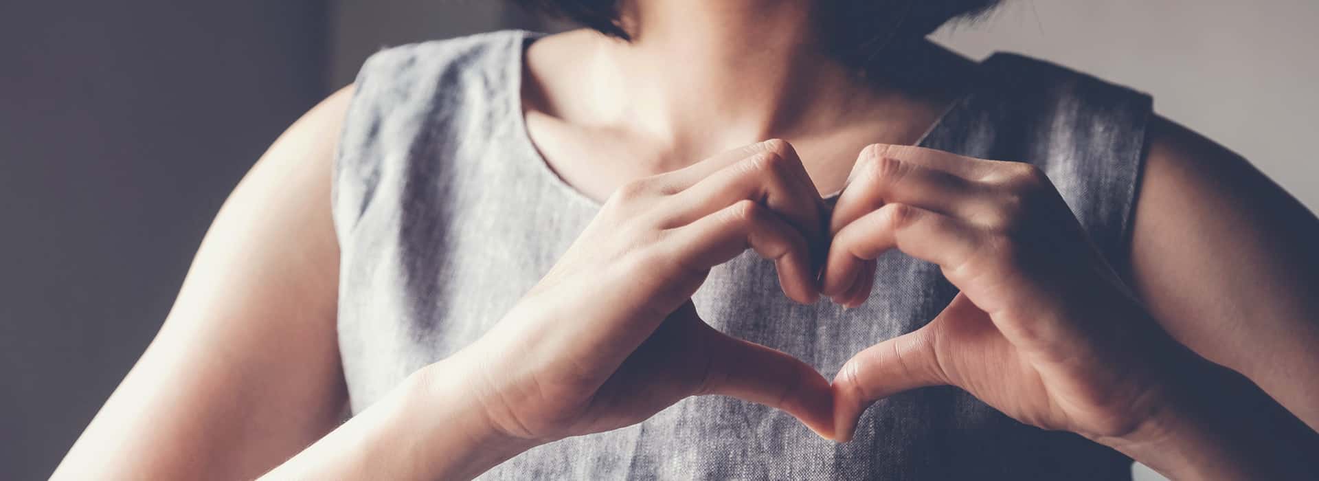 Eine Frau formt ein Herz mit ihren Händen vor der Brust