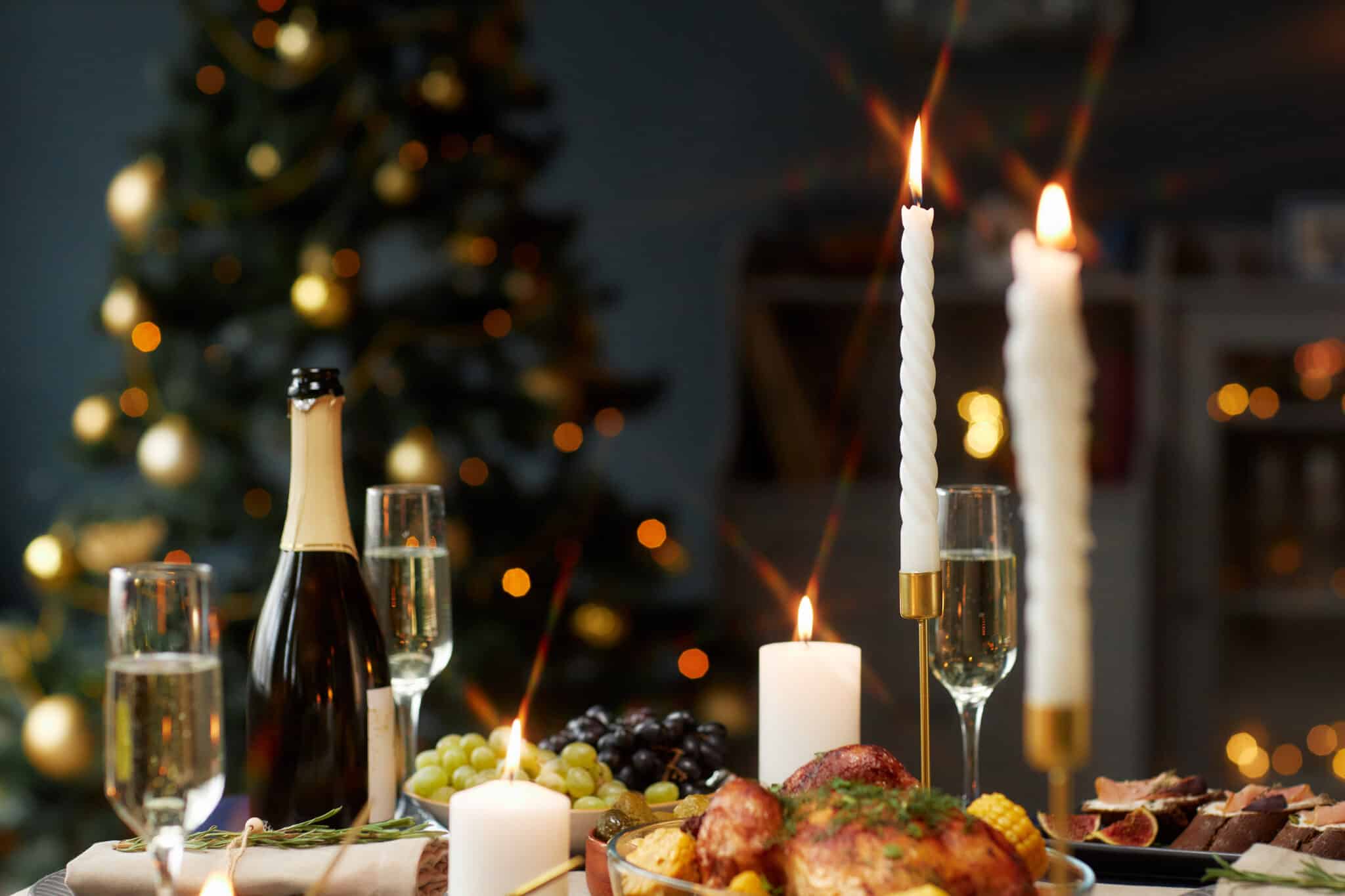 Ein festlich gedeckter Tisch mit Kerzen, Champagner, Trauben und einem Hähnchen.