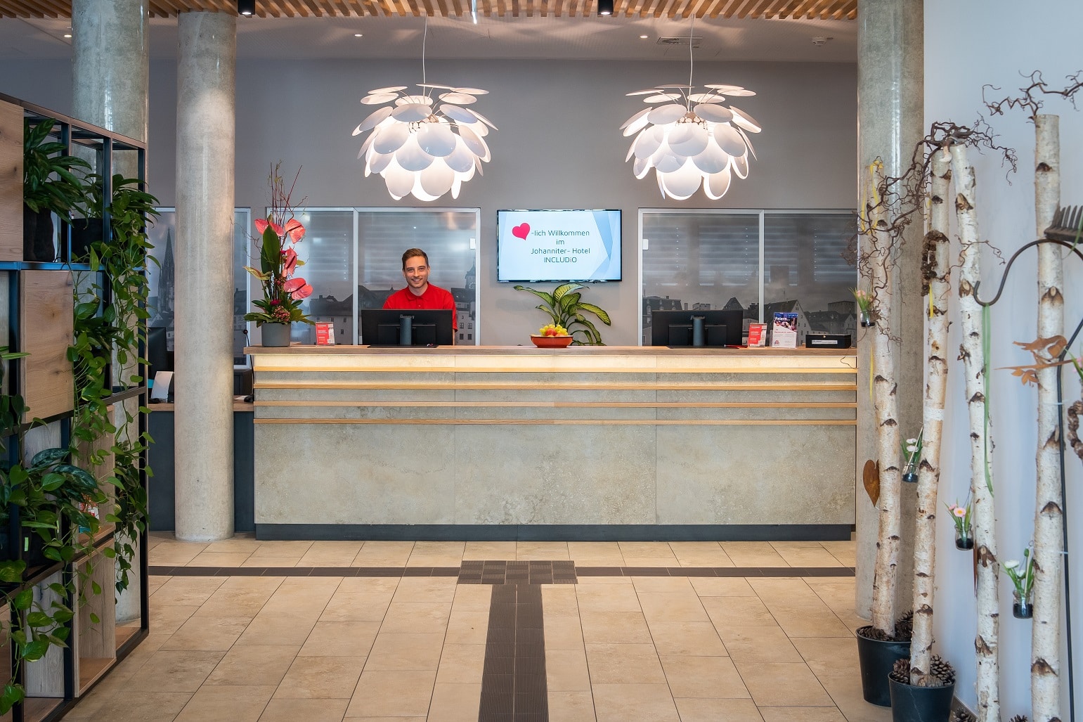 Rezeption im Hotel INCLUDiO mit einem Mitarbeiter und modernen Lampen.