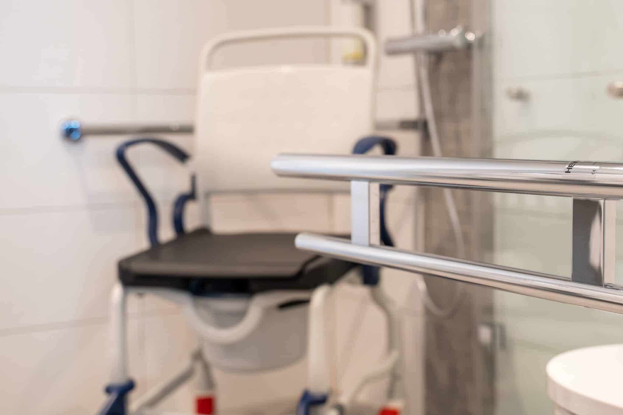 Duschstuhl mit schwarzem Sitz in einem Badezimmer, ausgestattet mit Haltegriffen und Duschbereich.