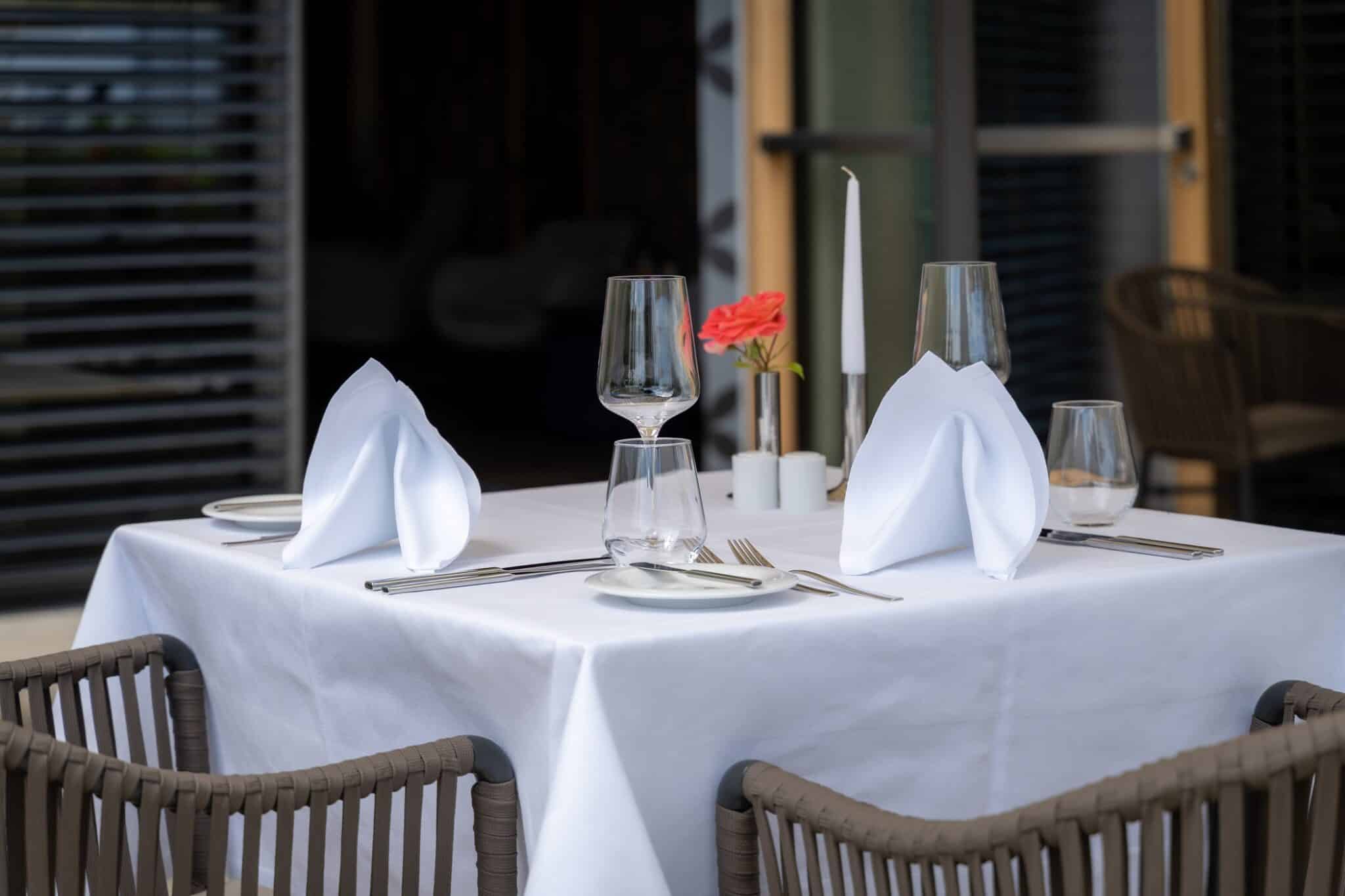 Eleganter Tisch mit weißer Tischdecke, Gläsern und Besteck in unserem Restaurant.