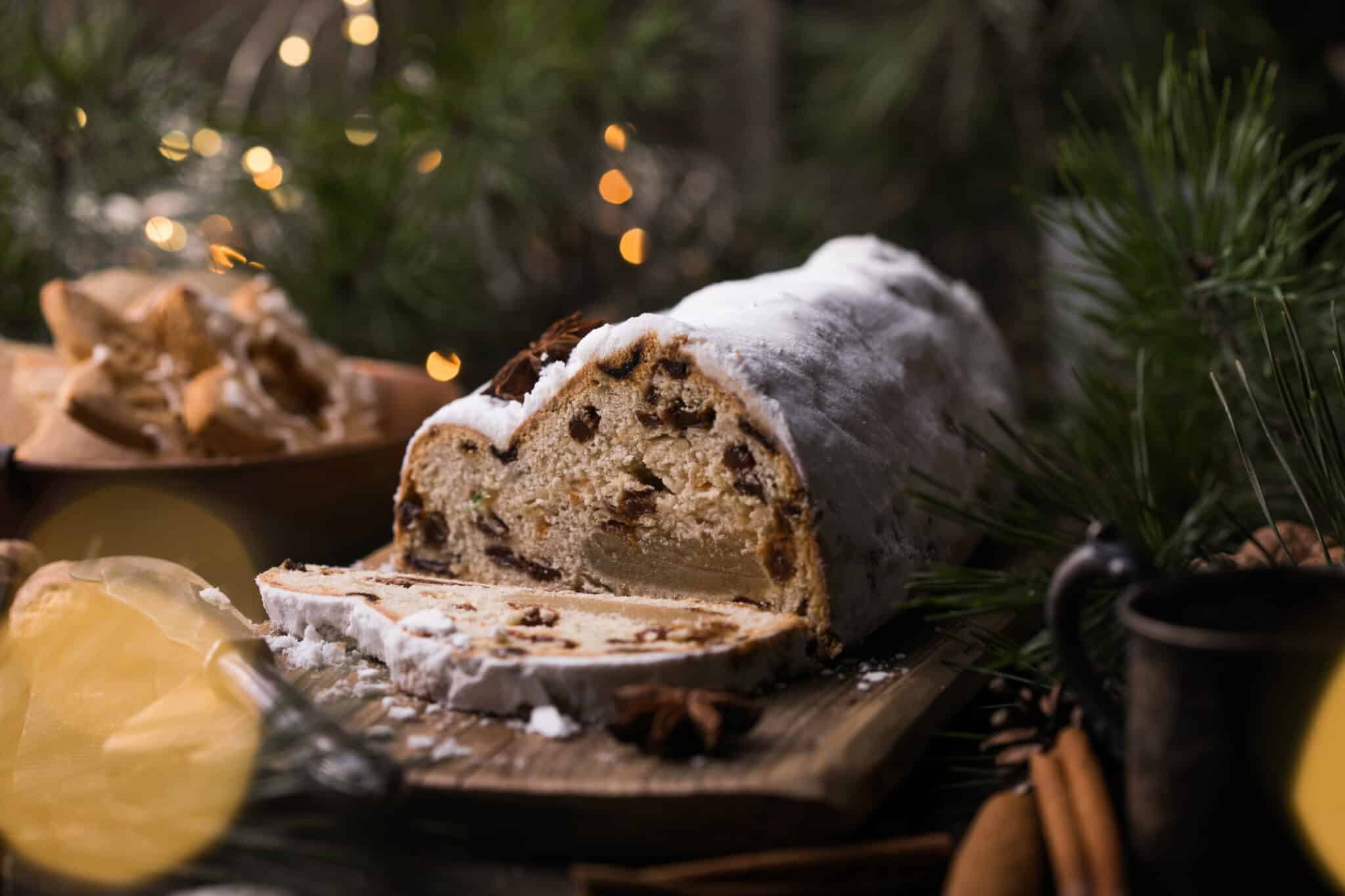 Traditioneller Weihnachtsstollen auf einem Holzbrett mit Puderzucker und Trockenfrüchten.